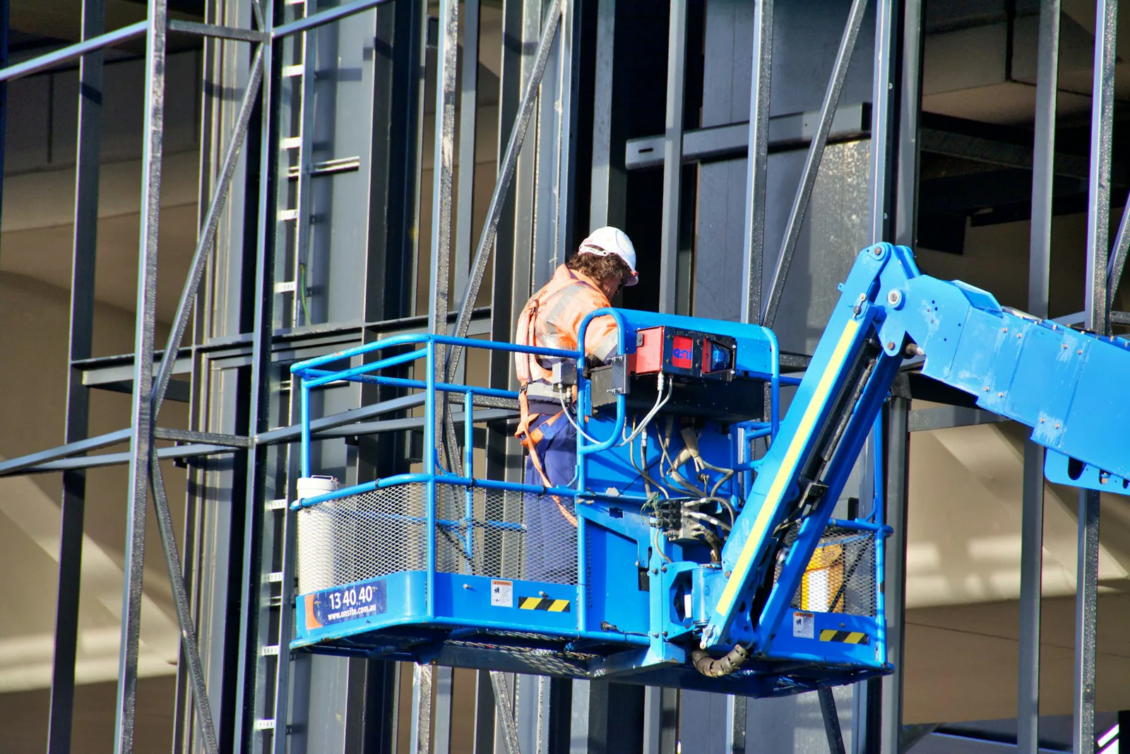 A construction worker on a lift against a steel building frame.